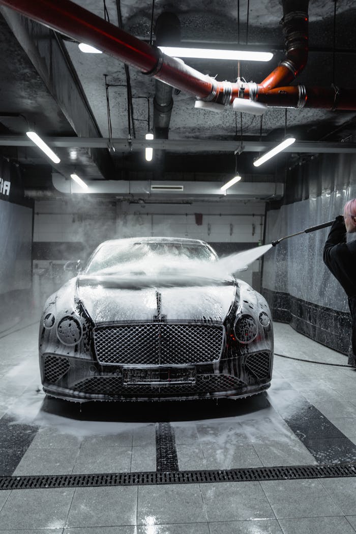 A Bentley Continental GT being washed with foam and a high-pressure hose in a car wash.